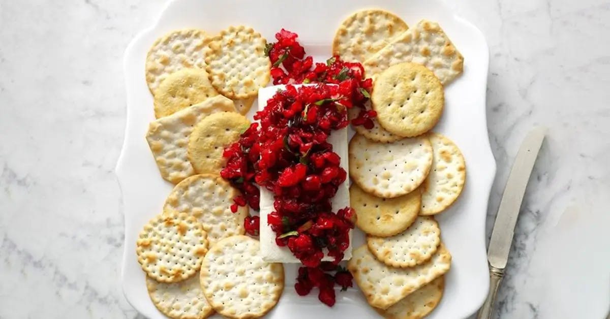 Holiday salsa on top of a block of cream cheese, surrounded by crackers.