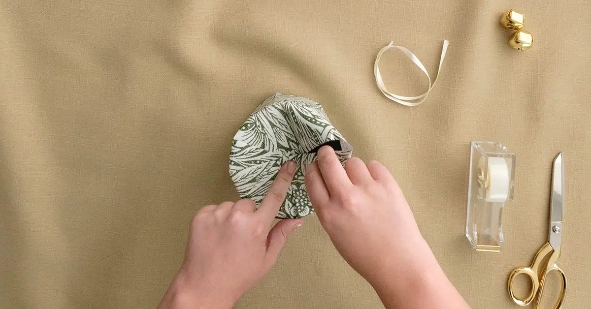 Making pleats in the wrapping paper at the top of a candle or cylinder.
