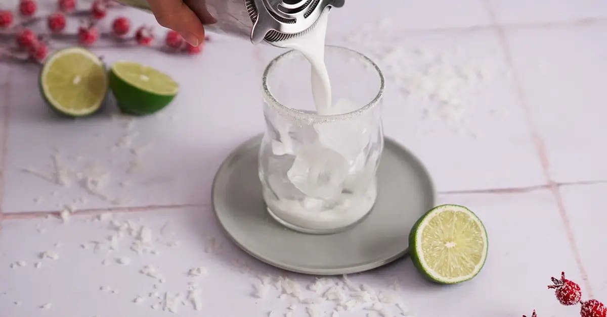Pouring a White Christmas Margarita cocktail into a glass.