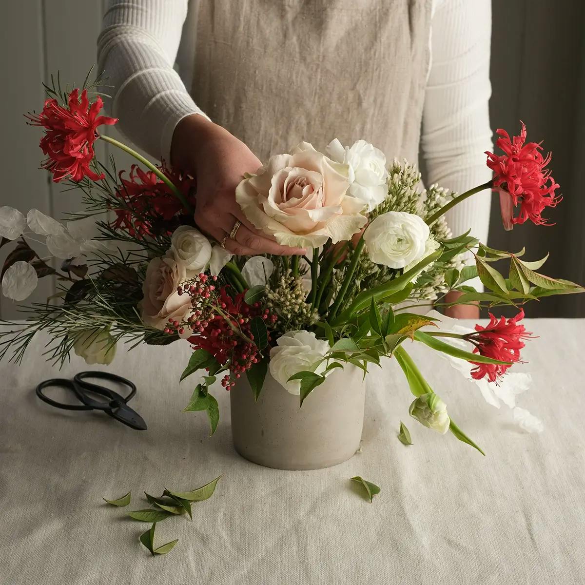 Hands adding flowers to a vase for a Christmas centerpiece.