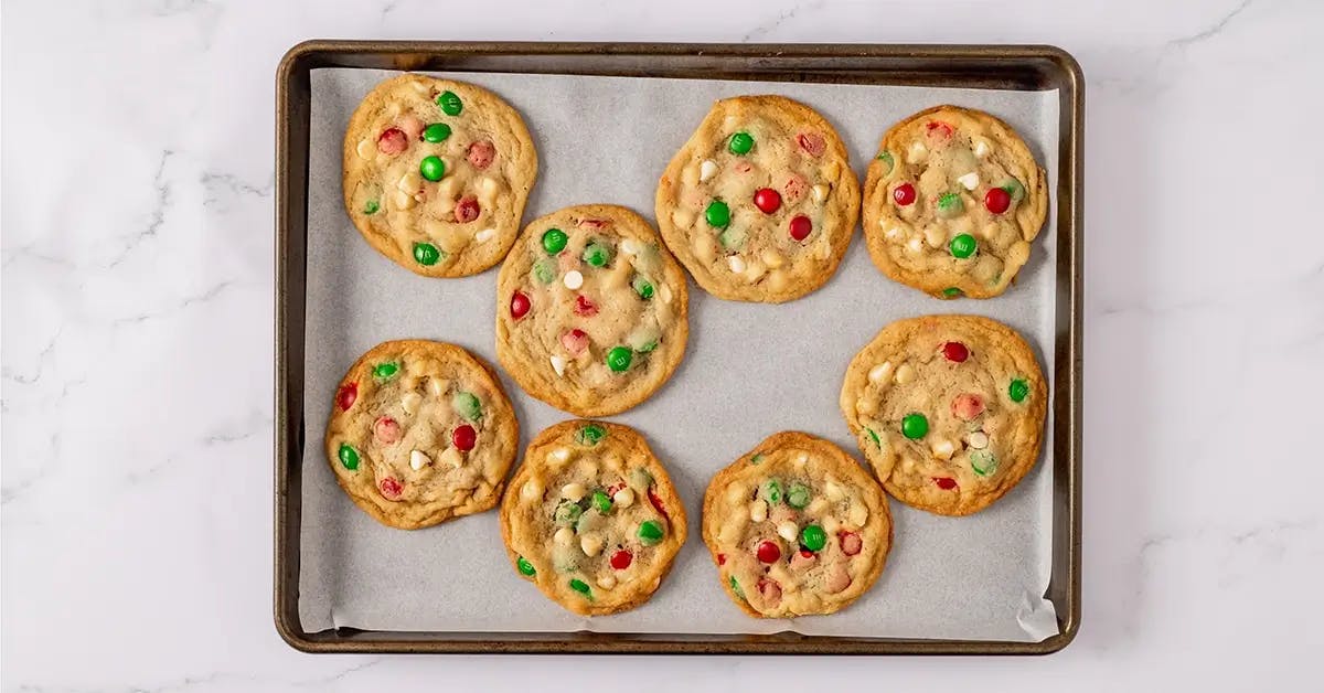 Christmas M&M cookies cooling on a baking tray lined with parchment.