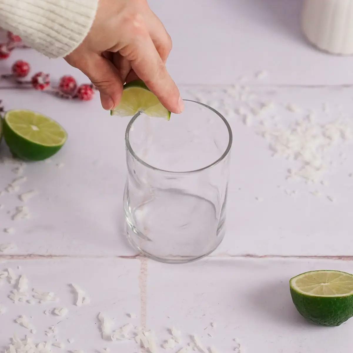 A hand using a lime to wet the rim of a glass ready for a Christmas margarita.