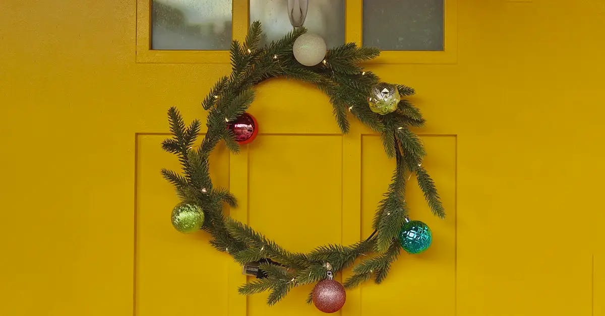 A contemporary yellow door with a simple wreath with primary-colored bulbs.