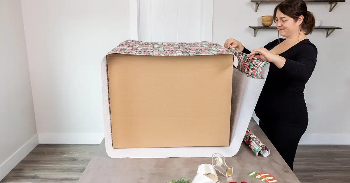Pulling a roll of SANTA.COM branded wrapping paper up to the edge of a large box.