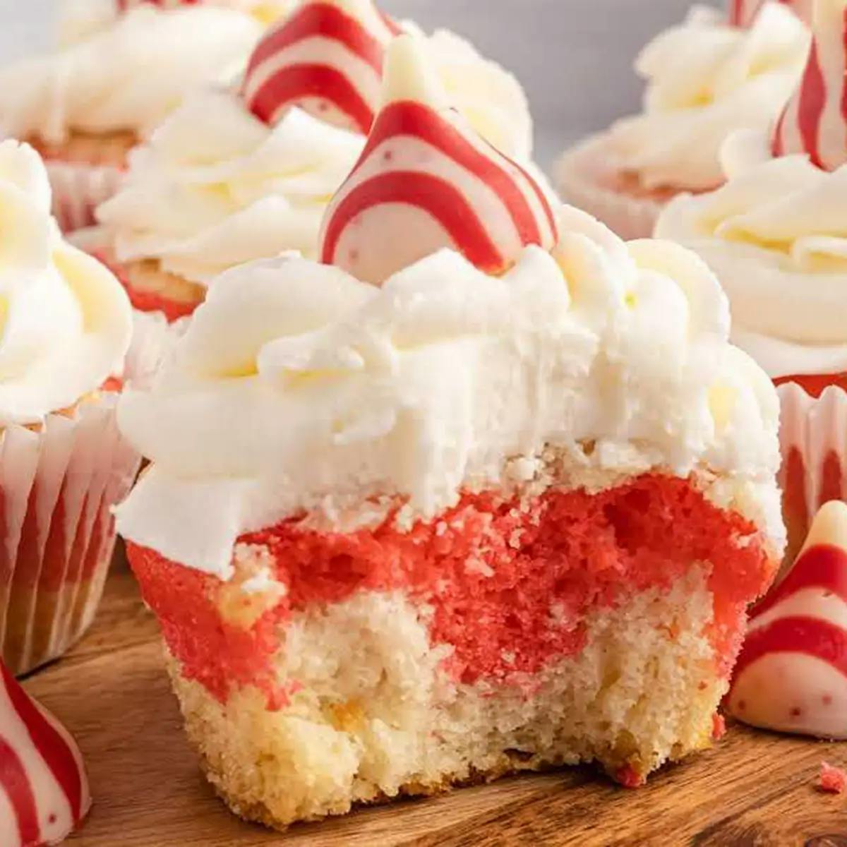 Red and white Christmas cupcake on cutting board, one with a piece taken out to reveal the striped inside of the cupcake. 
