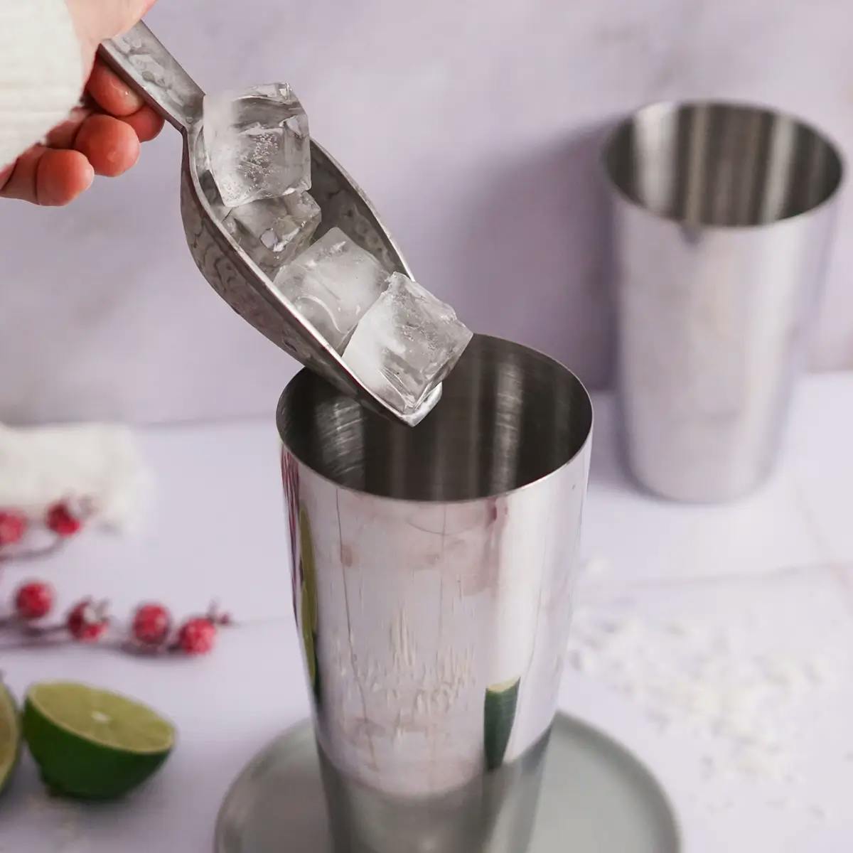 A hand adding ice to a shaker filled with the ingredients for a White Christmas Margarita cocktail.