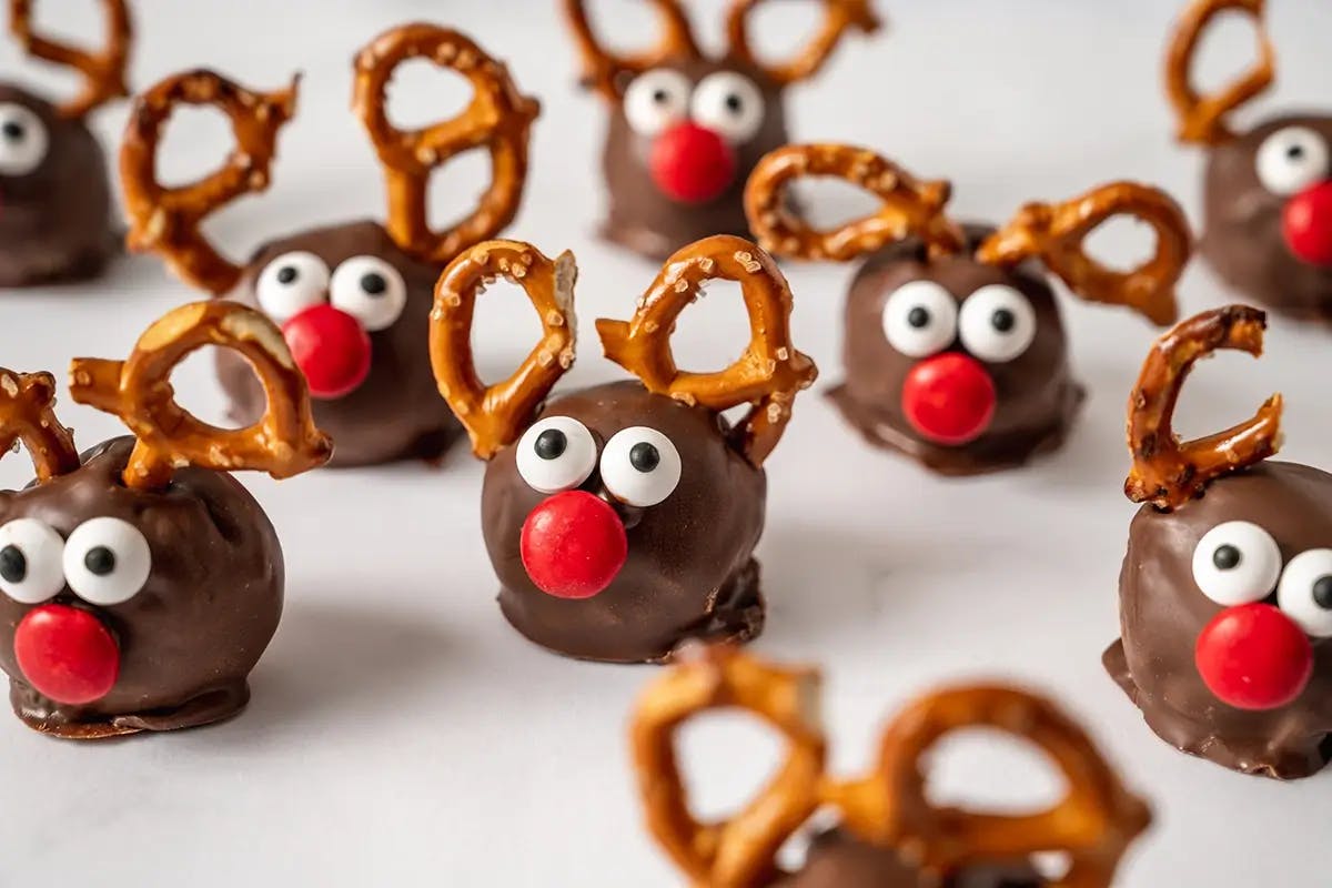 Reindeer Cookie Dough Bites covered in chocolate with pretzel pieces for antlers and mini M&Ms as eyes and nose.