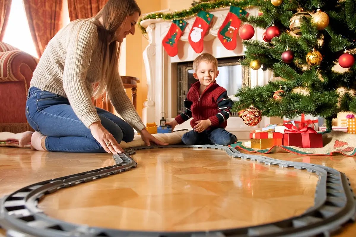 Mother and son play with model train set under Christmas tree.