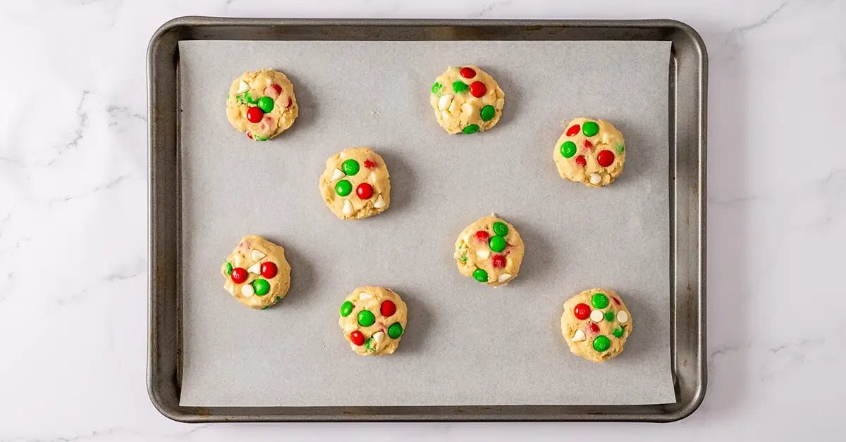 Christmas M&M cookie dough balls spaced out on a baking sheet, ready to go into the oven.