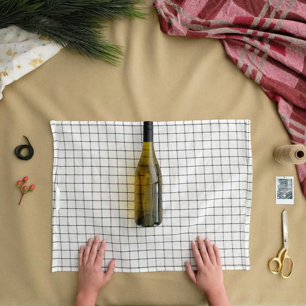Tutorial on how to wrap a wine bottle, showing step 1: laying the wind bottle on the tea towel.