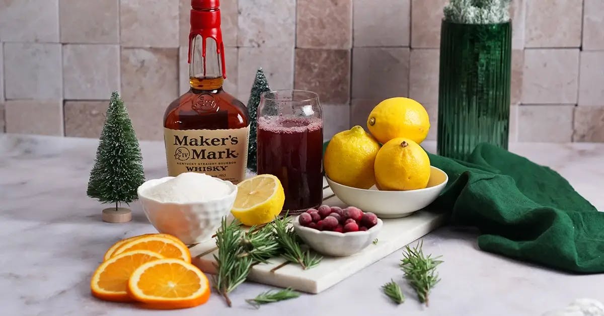 The ingredients for a Christmas punch recipe: Makers Mark bourbon, lemons, sugar, cranberries, and sliced oranges.