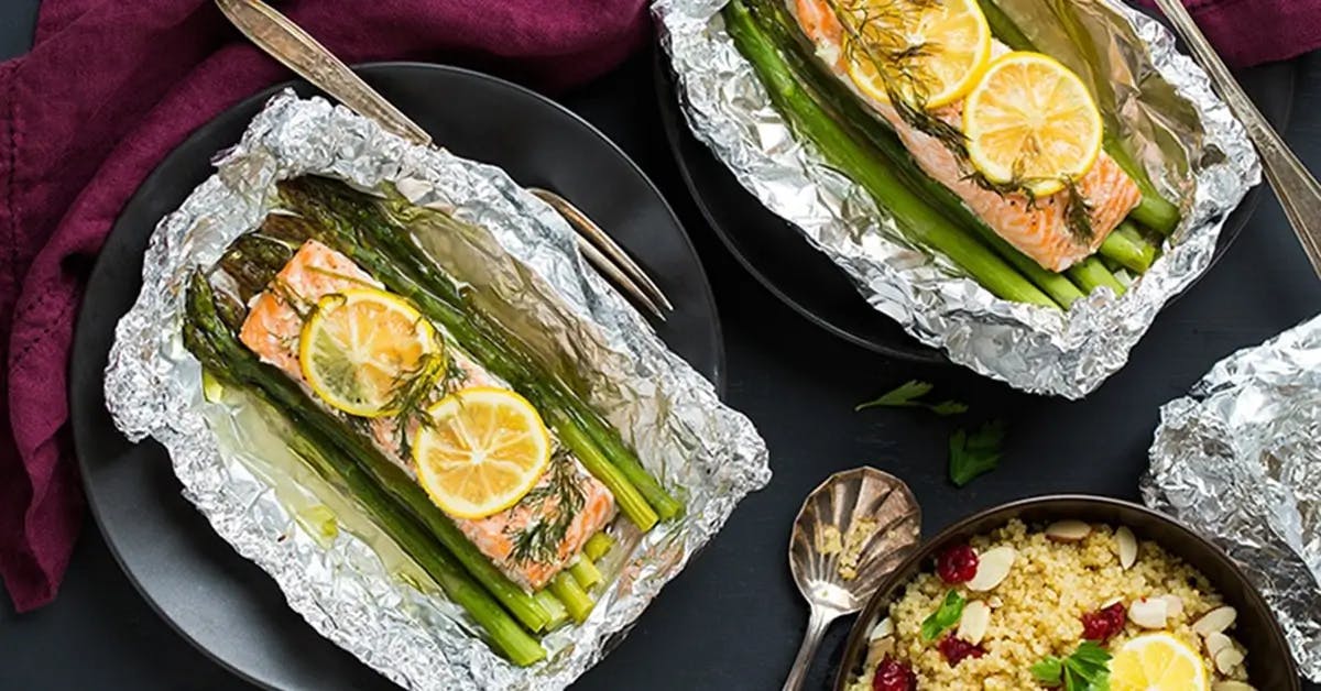 Romantic dinner recipe for two, showing salmon filets topped with lemon and dill, baked in foil on a bed of asparagus.
