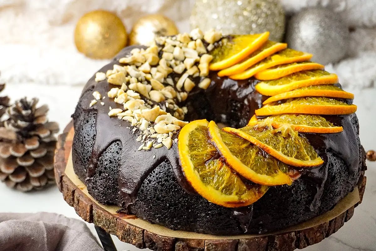 Vegan chocolate orange cake covered in vegan chocolate ganache and decorated with nuts and orange slices.