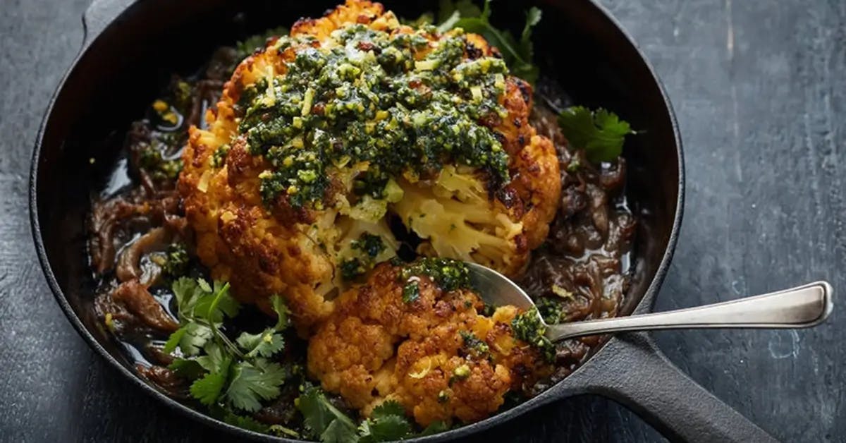 Whole roasted head of cauliflower in a skillet.