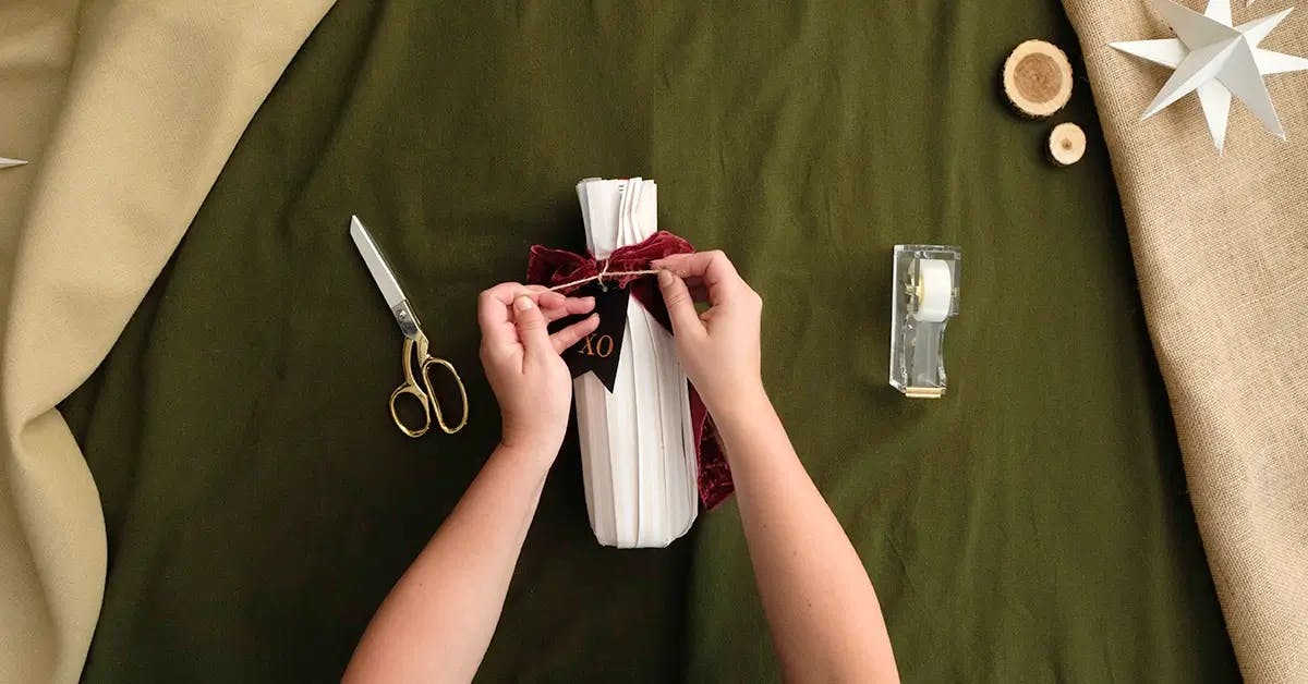 Tying a tag to a wine bottle wrapped in pleats.