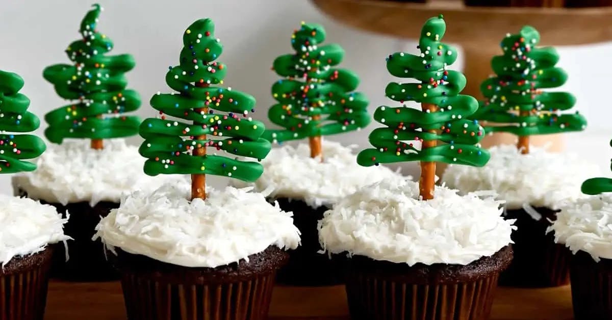 Chocolate cupcakes topped with mounds of white frosting and a beautiful, frosting sculpted Christmas tree sprinkled with multi-colored sprinkles.