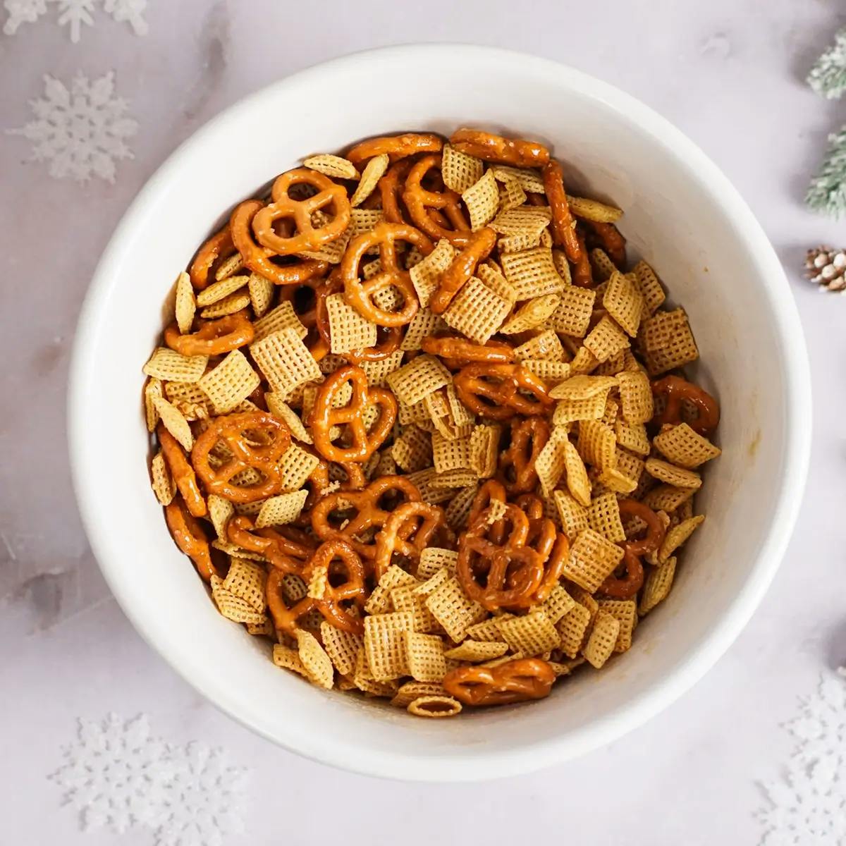 Cereal, pretzels and butter in a bowl being prepared for a Christmas Chex Snack Mix.