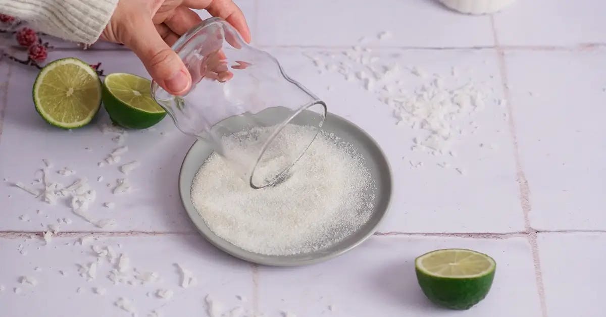 A hand rolling a glass in sugar to coat the rim, in a recipe for a Christmas Margarita.