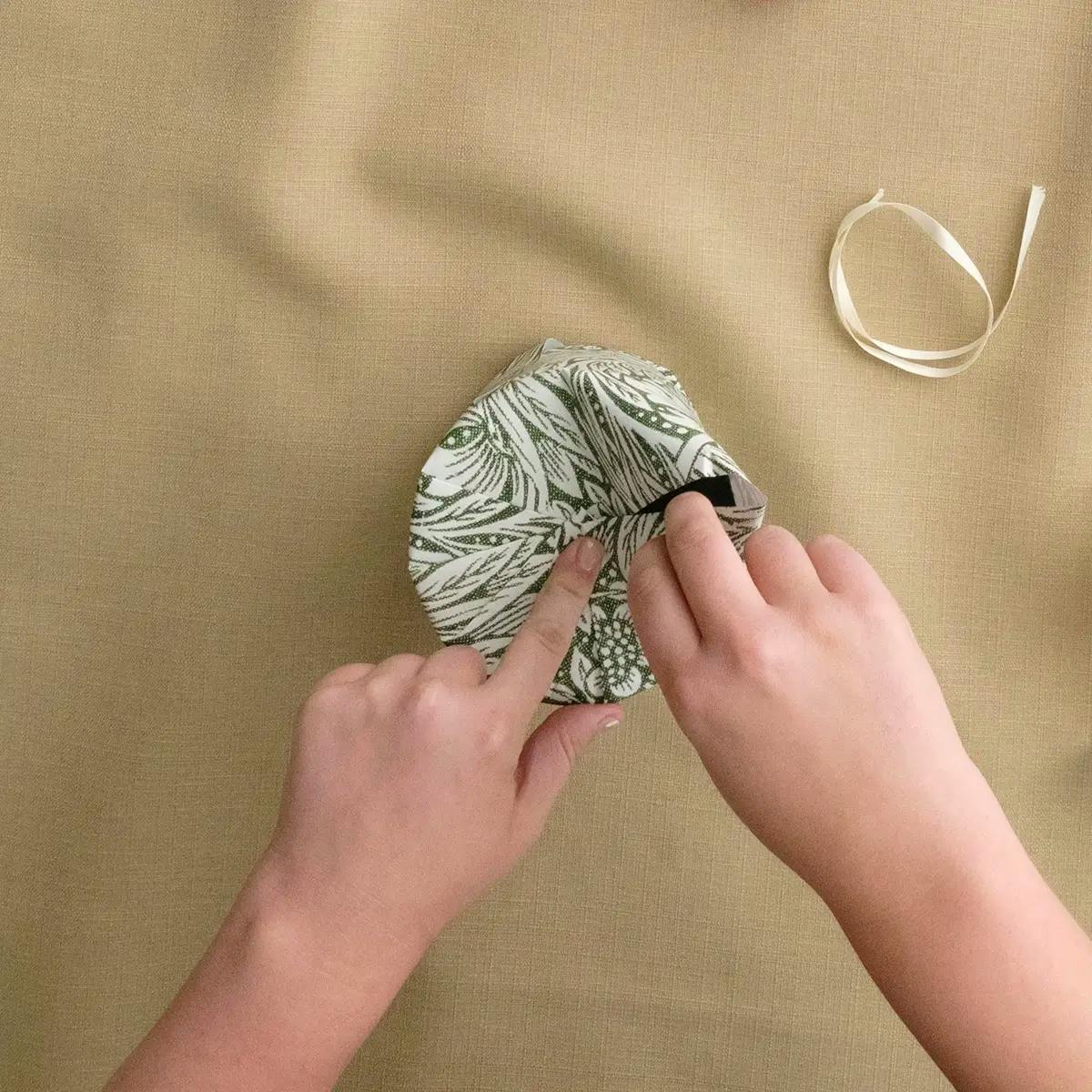 Making pleats in the wrapping paper at the top of a candle or cylinder.