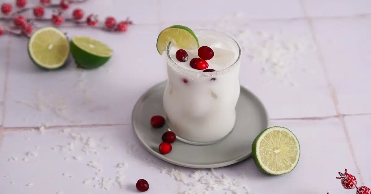 A White Christmas Margarita holiday cocktail in a glass, garnished with cranberries and a lime wedge.
