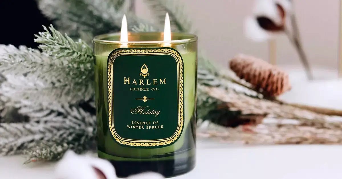 “Holiday” Christmas candle by The Harlem Candle Company, with fir branches in the background.