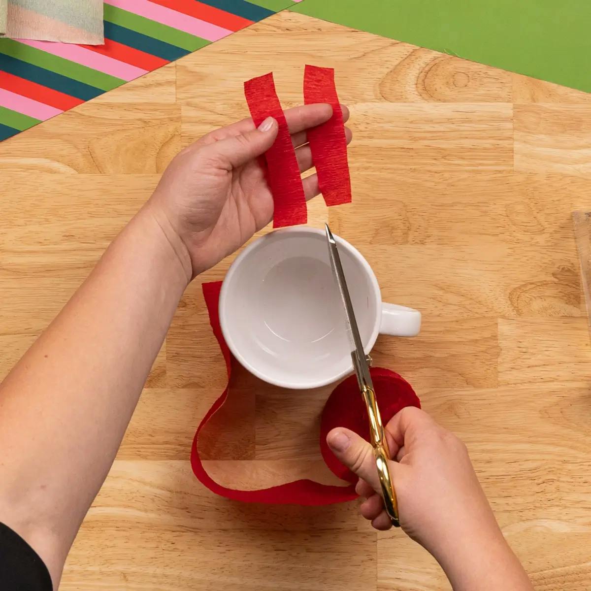Cutting strips of crepe paper to cover the handle of a mug, as part of a tutorial on how to wrap a mug or coffee cup.