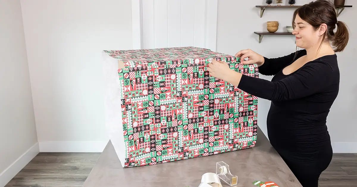 Securing wrapping paper to a large box with tape.