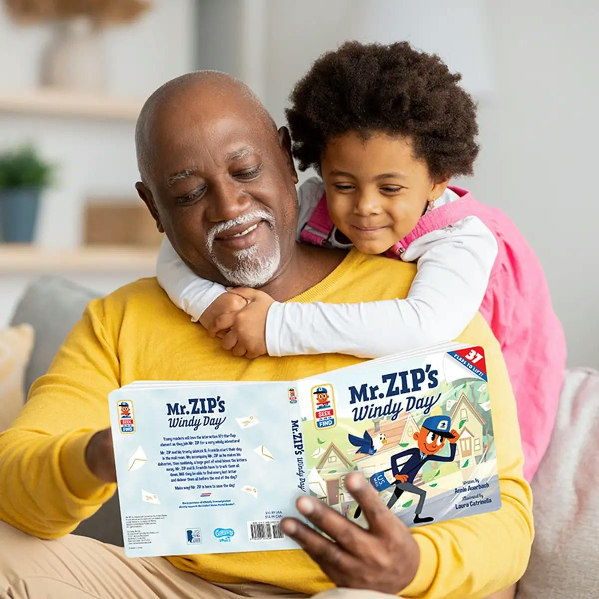African American man reading “Mr. ZIP’s Windy Day” to his granddaughter.