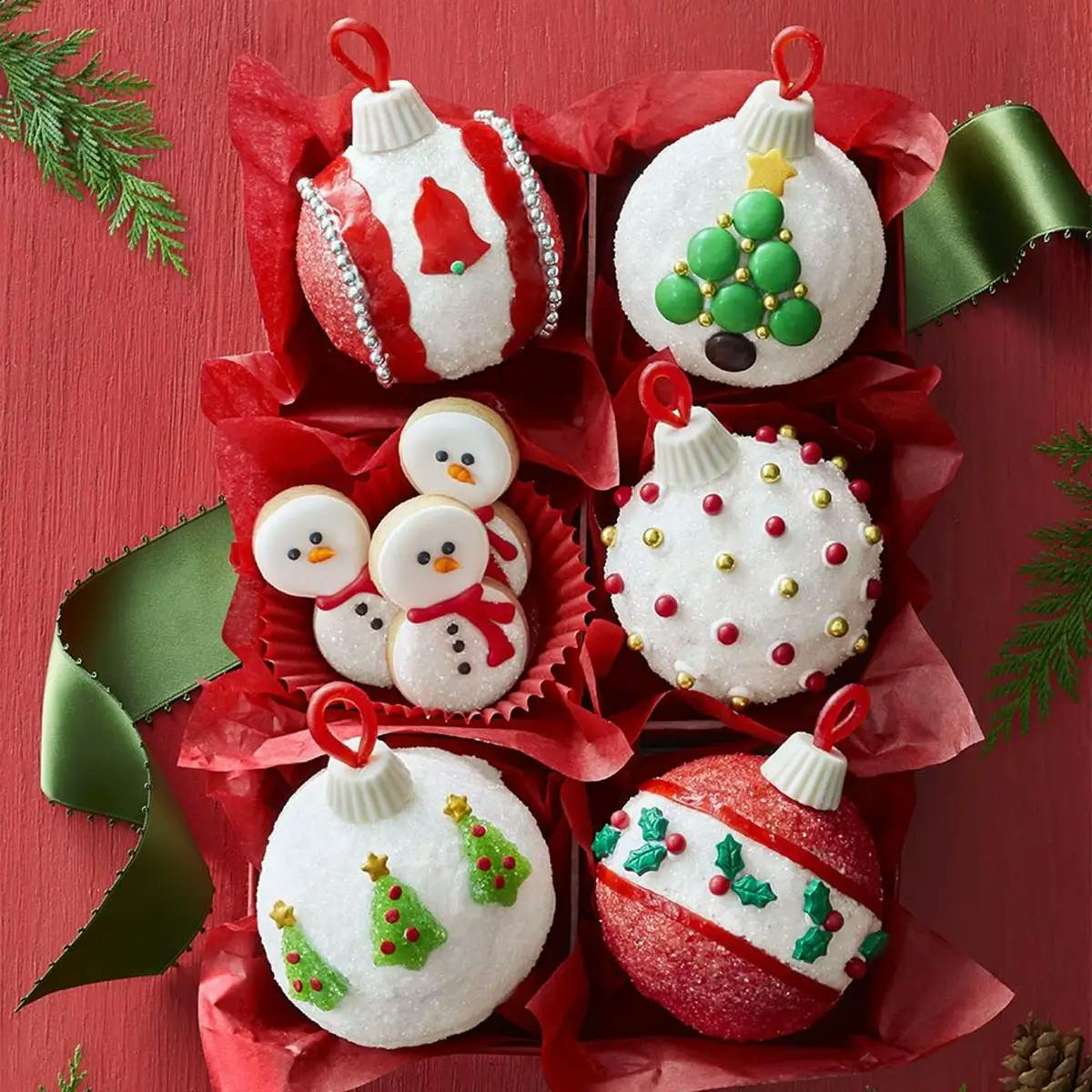 A box of red tissue-paper filled, Christmas cupcake ornaments in red, white and green, sparkling with holiday colors and adornments flanked by a loose green ribbon.