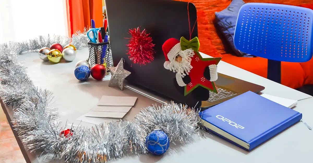 Decorated laptop with ornaments hanging off of computer, decorated pencil holder and garland and ornaments covering desk surface.