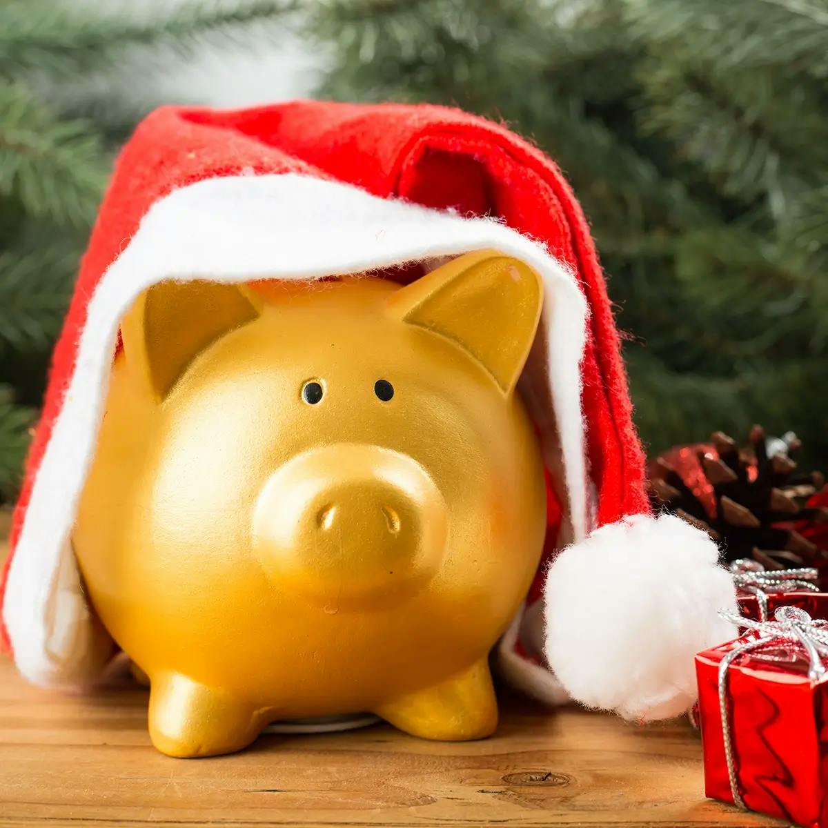 Gold piggy bank wearing a Santa hat with Christmas gifts. Illustration for an article on managing Christmas on a budget.