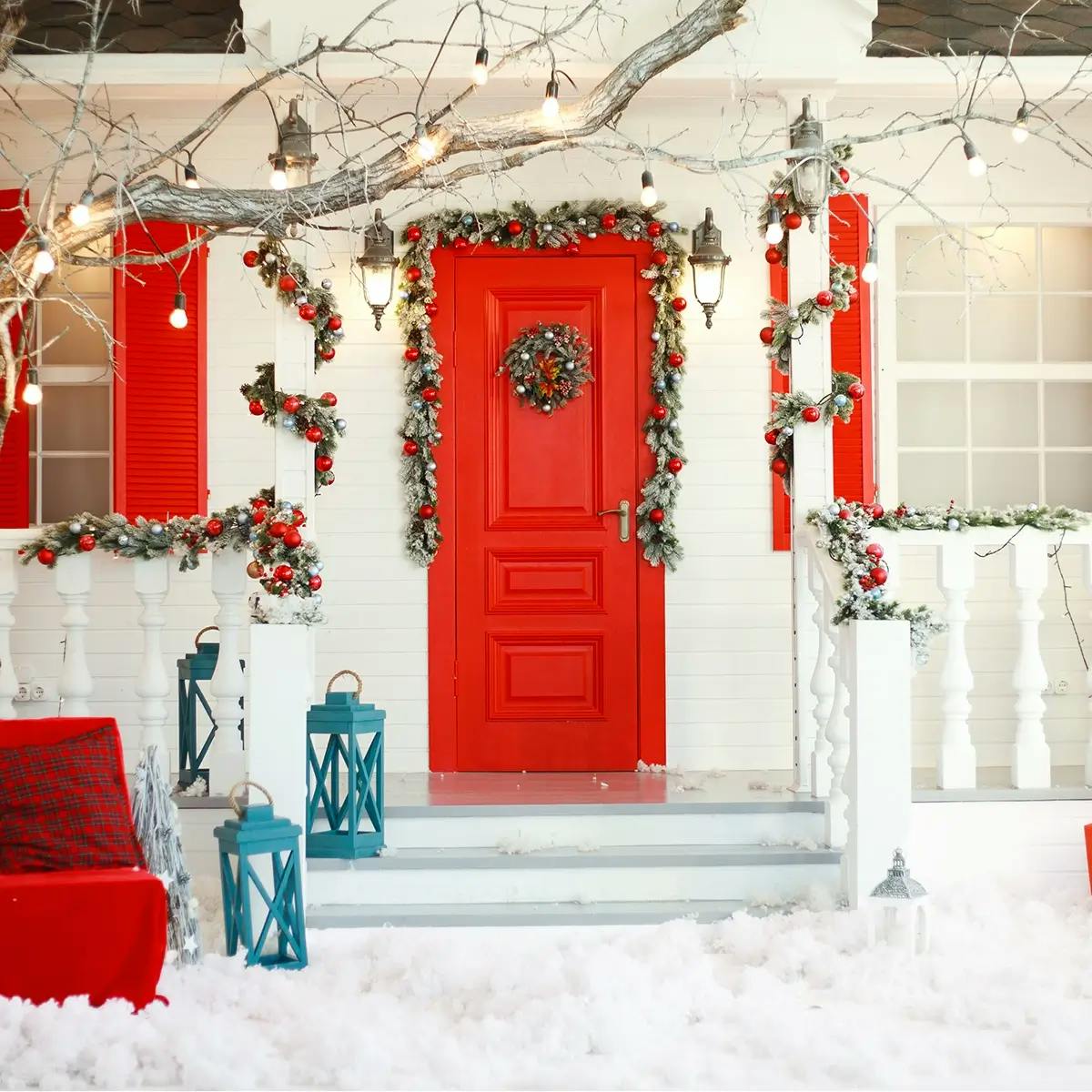 Festive white house with red door, garland over door, with a red bench in front with pillows.