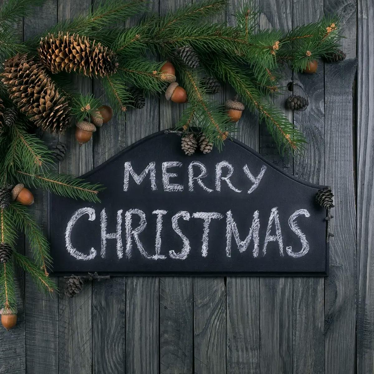 “Merry Christmas” written on chalkboard and hung on front door as part of Christmas porch decorations.