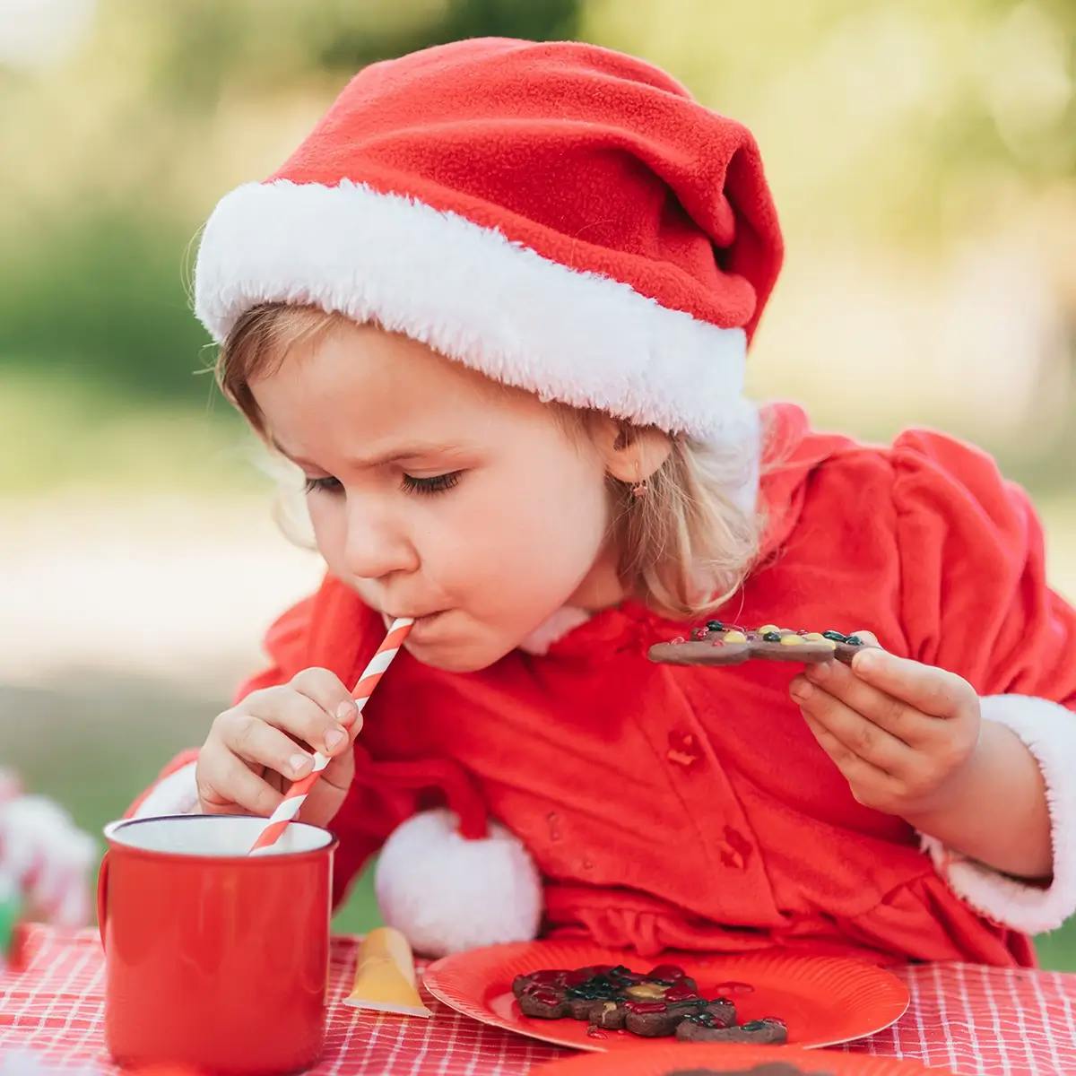 Young girl dressed in holiday clothes and drinking hot chocolate during Christmas in July celebration.