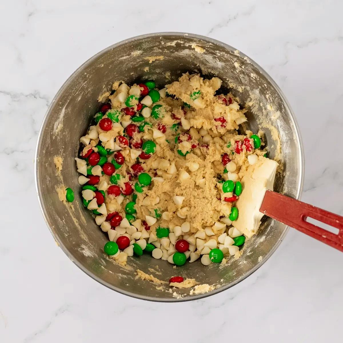 Christmas M&M cookie dough in a bowl with a spatula, after white chocolate and red and green M&Ms have been mixed in.