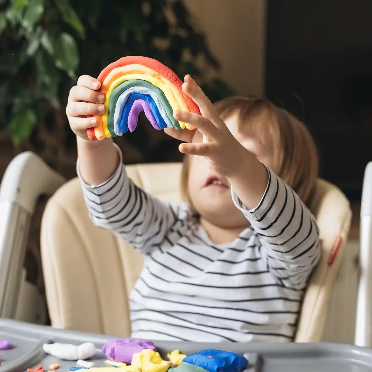 Young child holding a rainbow made from modeling clay for St Patrick’s Day crafts.