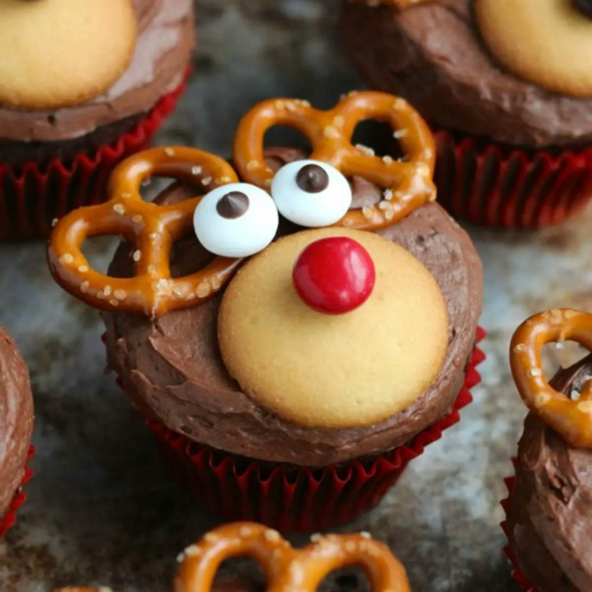 A vanilla cupcake decorated to look like a reindeer, two pretzels as ears, frosting for the eyes, and a red gum ball for the nose.