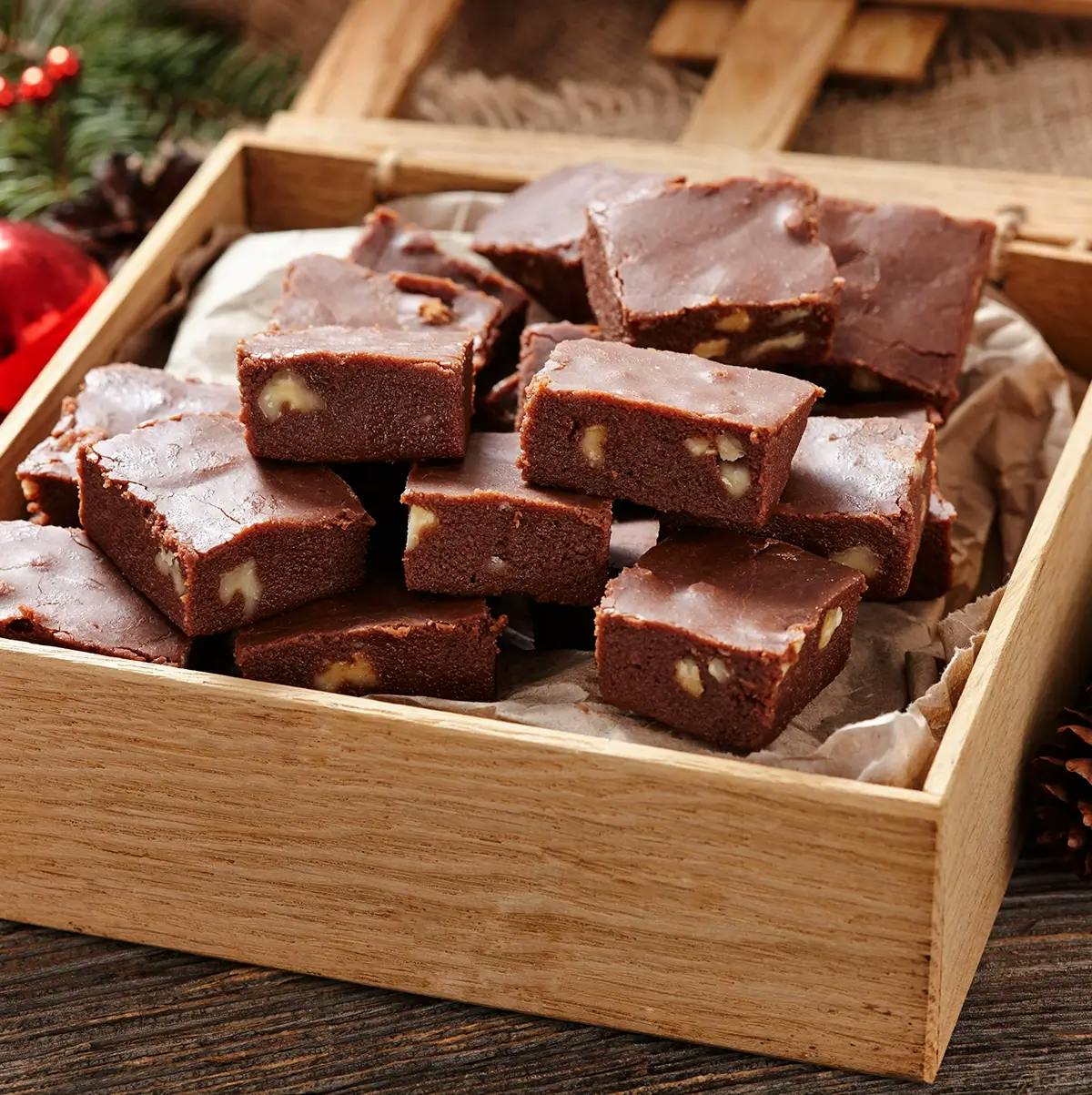 Chocolate microwave fudge with nuts in a box surrounded by Christmas ornaments and pinecones.