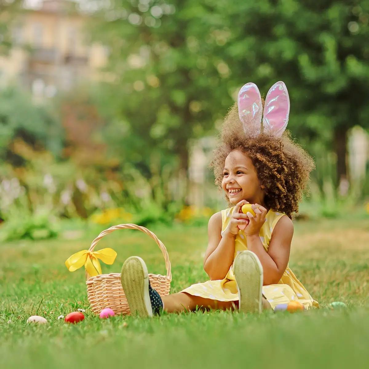 Young girl wearing bunny ears and holding an easter egg, next to easter basket.