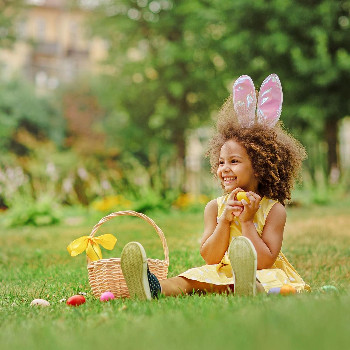 young girl wearing bunny ears and holding an easter egg, next to easter basket