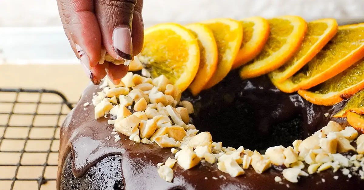 Fingers garnishing a vegan chocolate orange bundt cake with orange slices and nuts.
