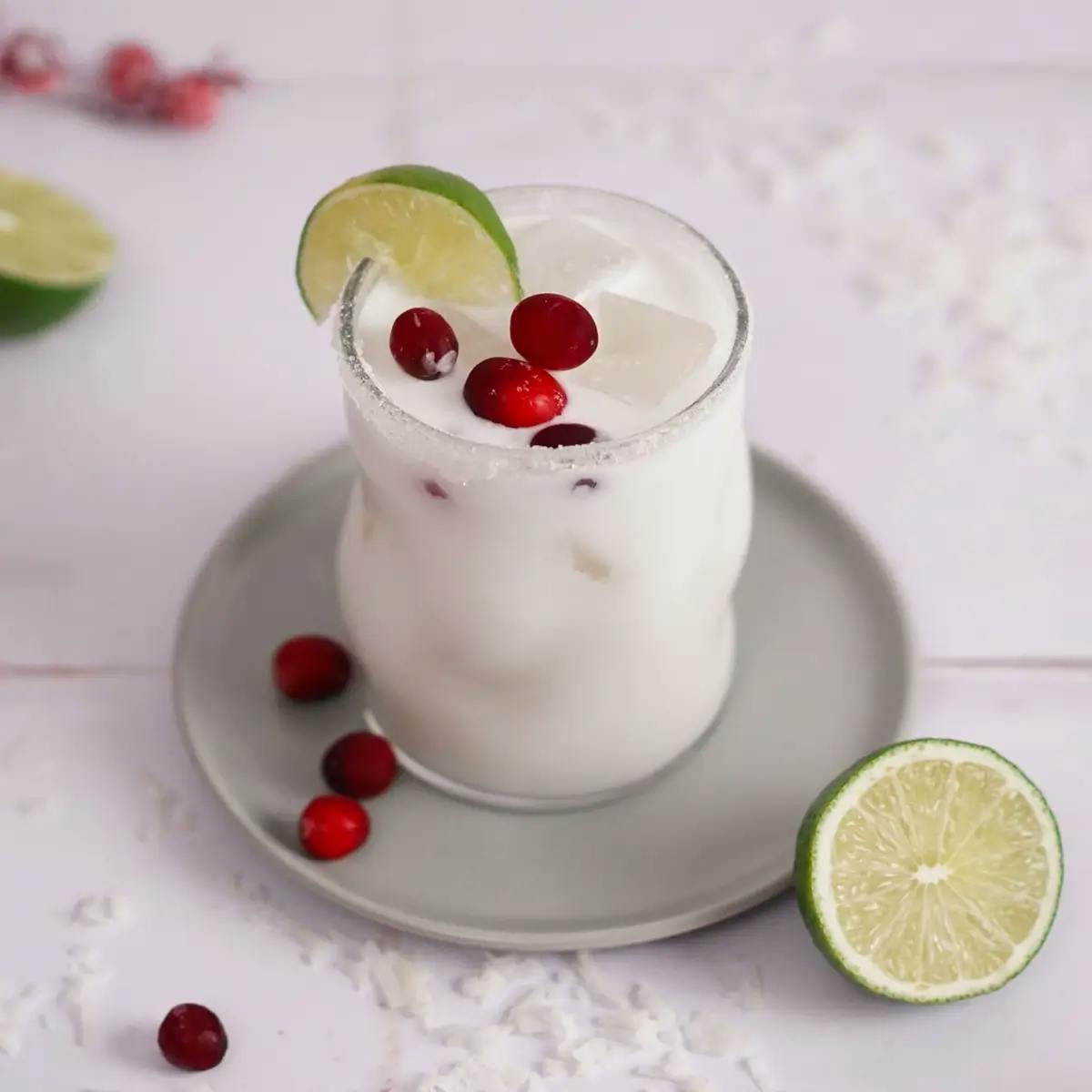 A White Christmas Margarita drink in a glass, garnished with cranberries and a lime wedge.