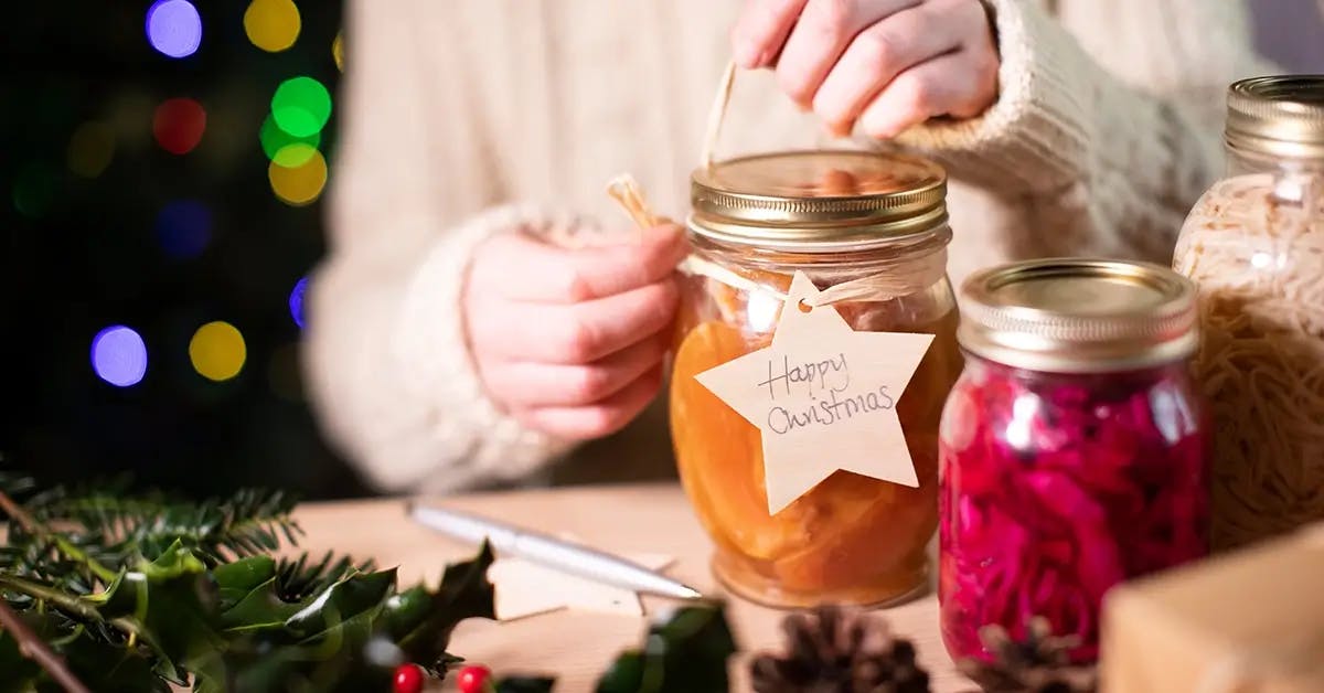 Hands tying a reusable wooden gift tag on homemade jars of preserves for a handmade Christmas gift on a budget.