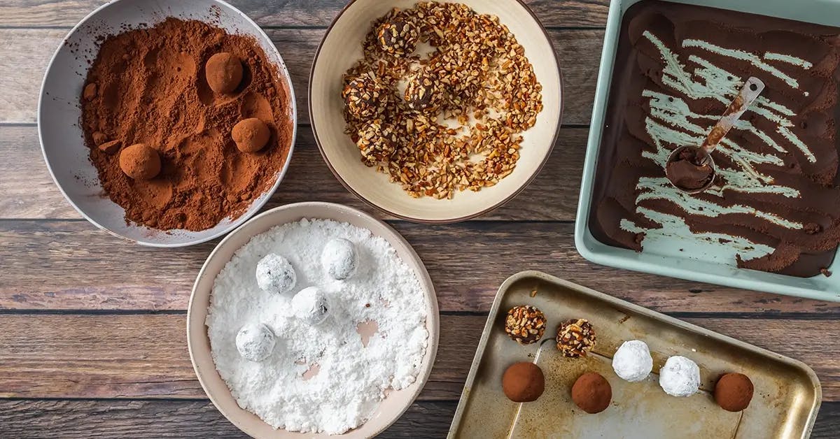 Rolling chocolate truffles into toppings and transferring them to a baking sheet. 
