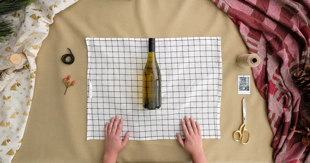 Tutorial on how to wrap a wine bottle, showing step 1: laying the wind bottle on the tea towel.