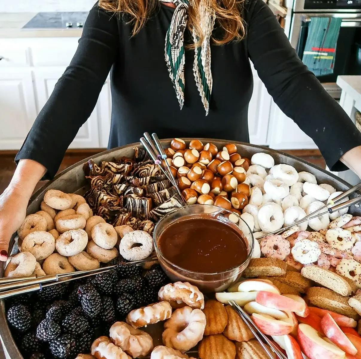 A Christmas dessert charcuterie board containing Nutella fondant dip with fruit, donuts, biscotti, and pretzels for dipping.