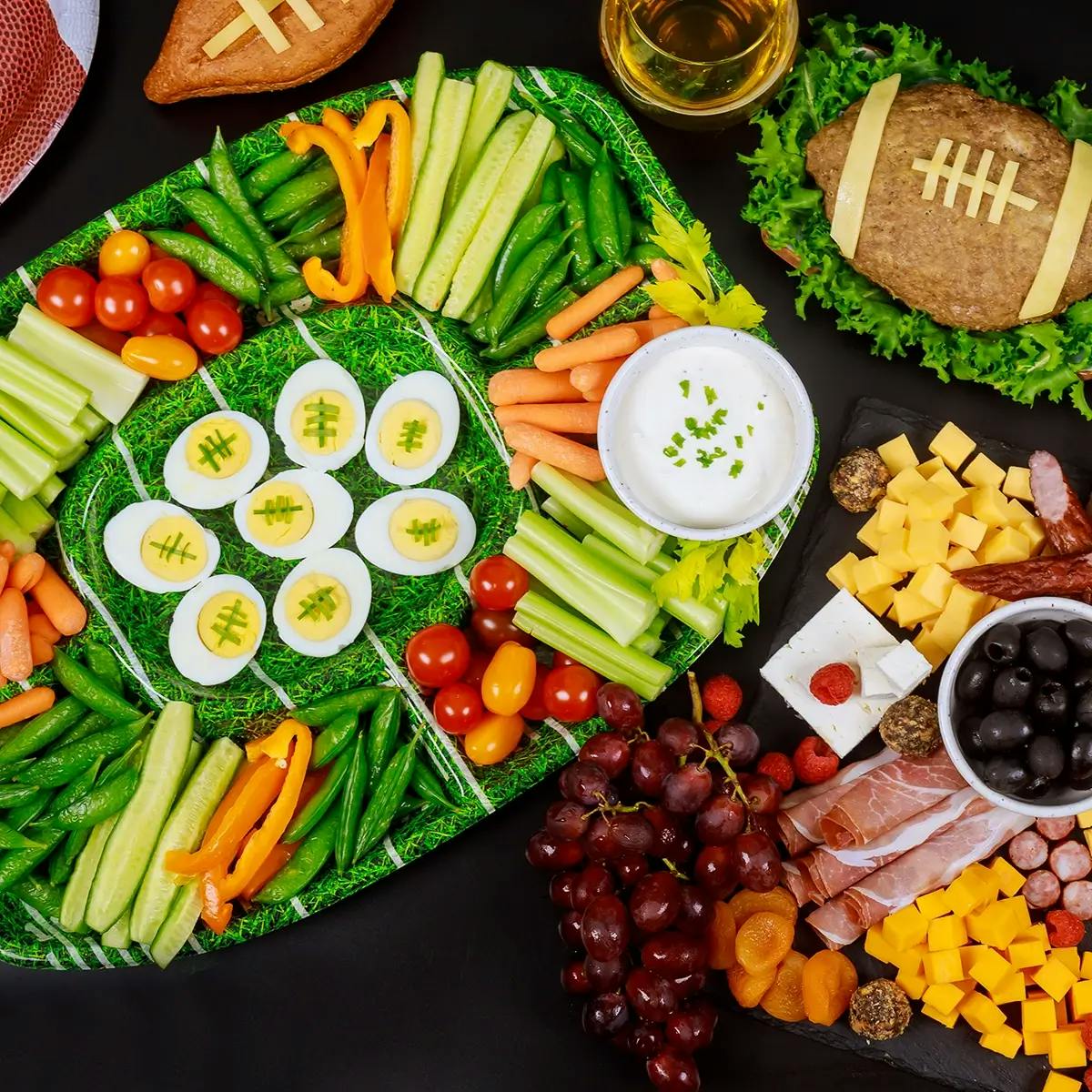 Super Bowl party snacks, including cheese, crackers, dried fruit, deviled eggs, and a vegetable platter that looks like a football field.