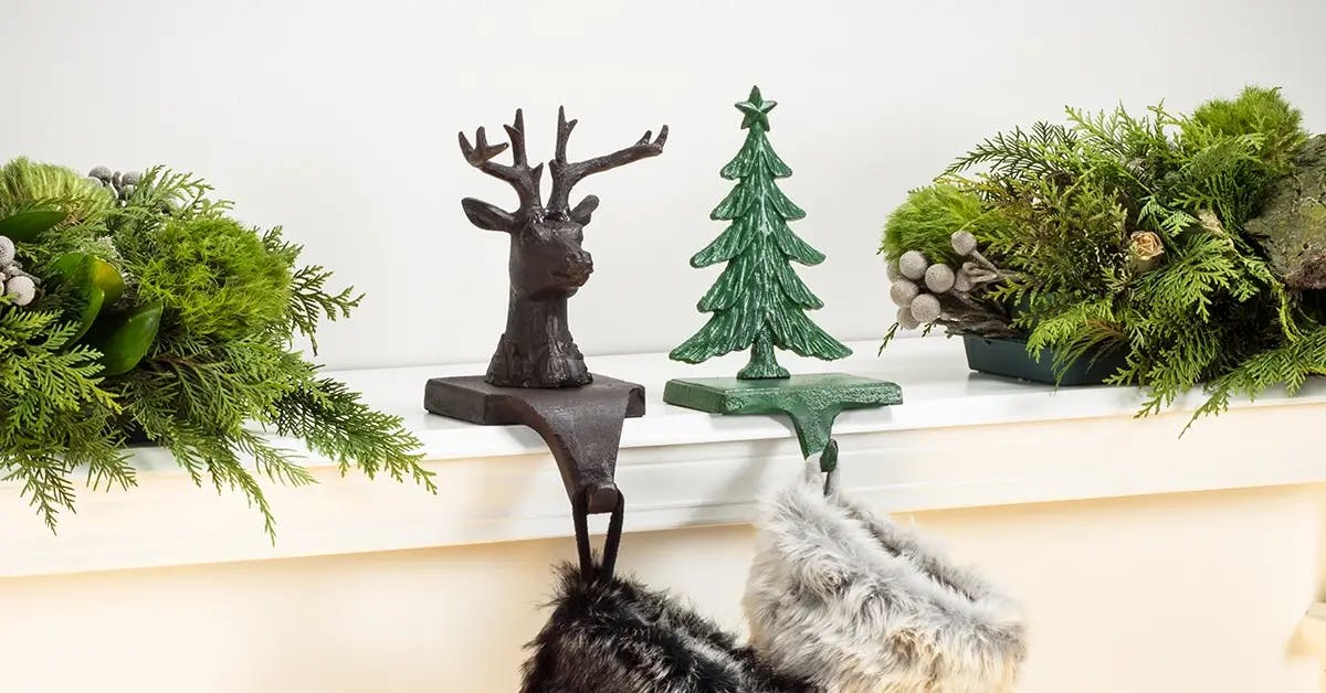 A black reindeer and green Christmas Tree holder, on a mantel holding two stockings over a white fireplace.