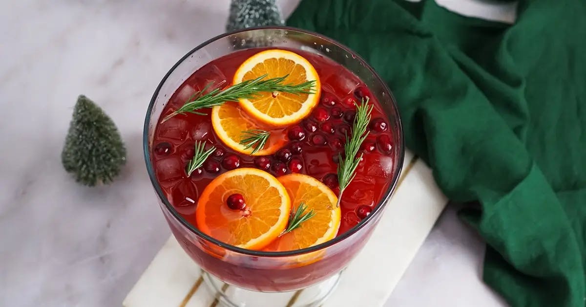 A bowl of Christmas punch, with orange slices and rosemark springs floating on top.