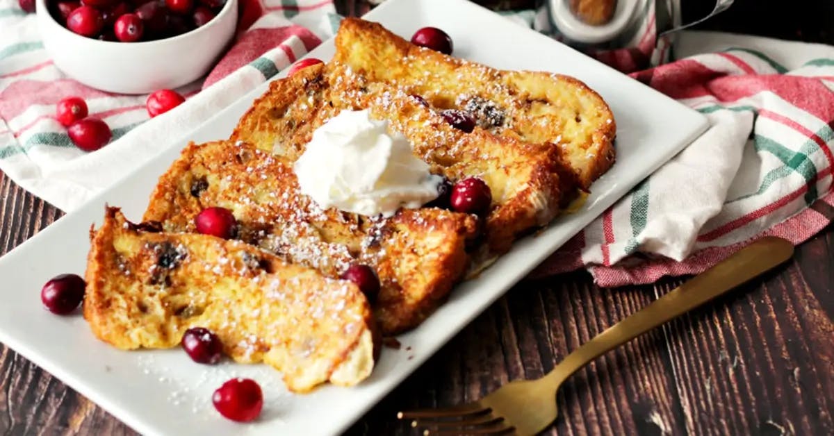 French toast made from panettone on a plate topped with cranberries and whipped cream.
